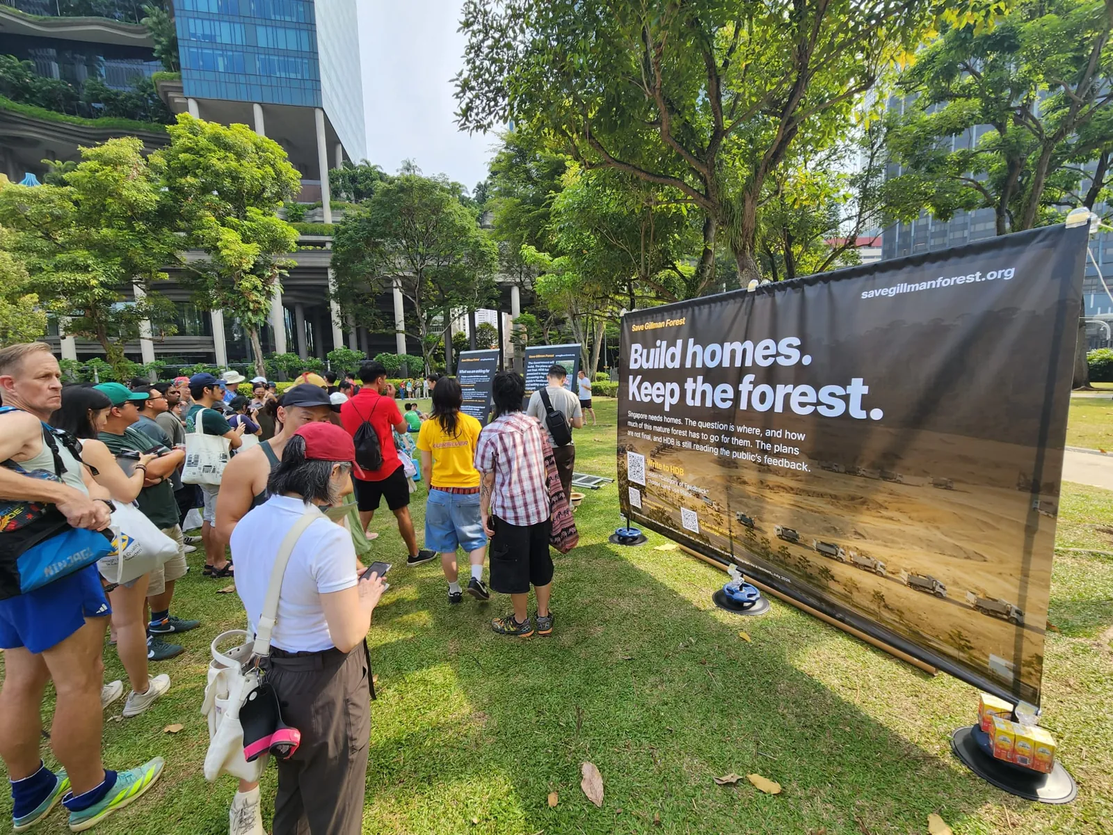 A Save Gillman Forest banner reading Build homes. Keep the forest. standing on the lawn as people walk past