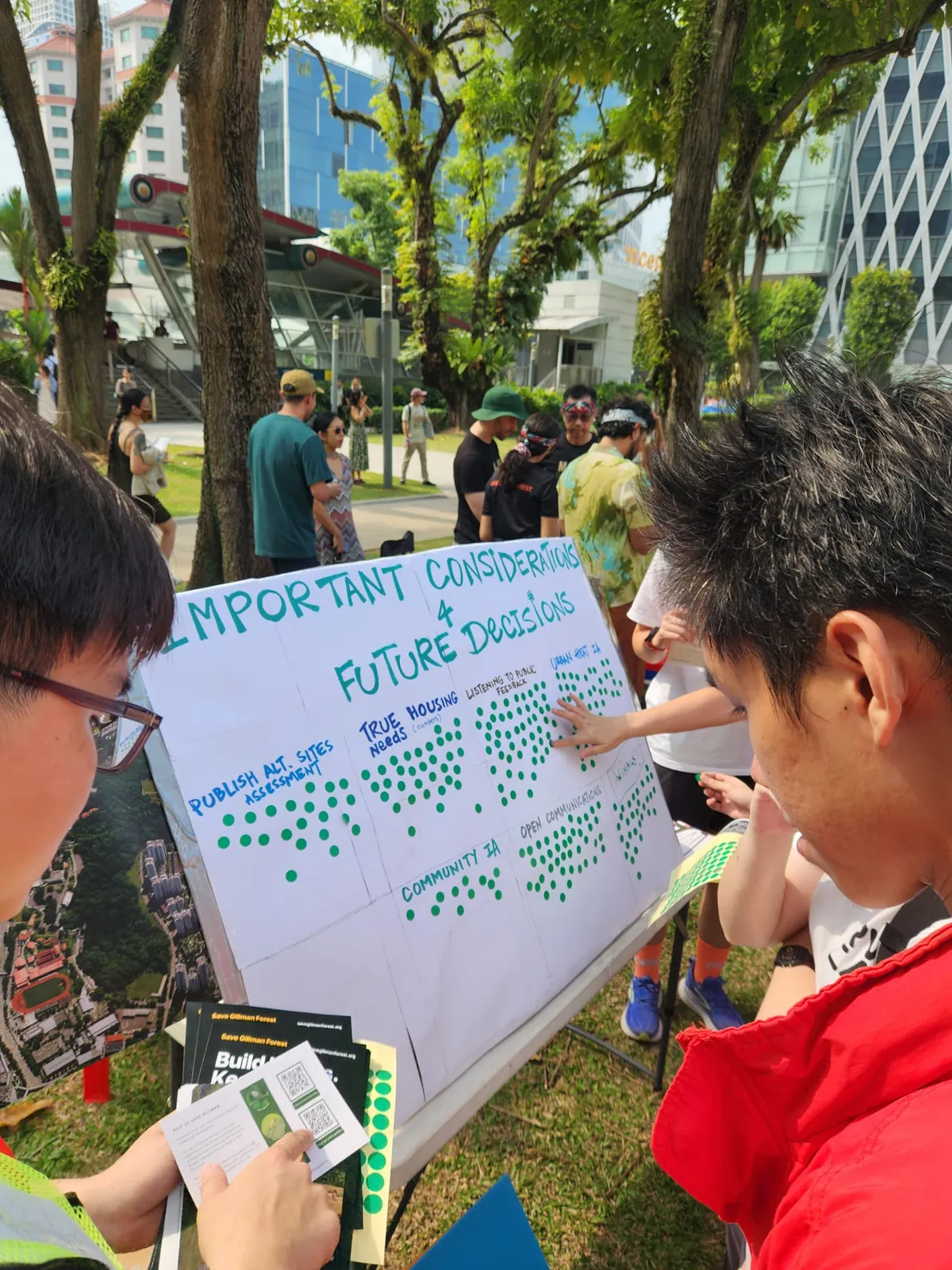 People placing green dot stickers on a board titled Important Considerations for Future Decisions, with columns for publishing alternative sites assessments, true housing needs, listening to public feedback, urban heat, community impact and open communications