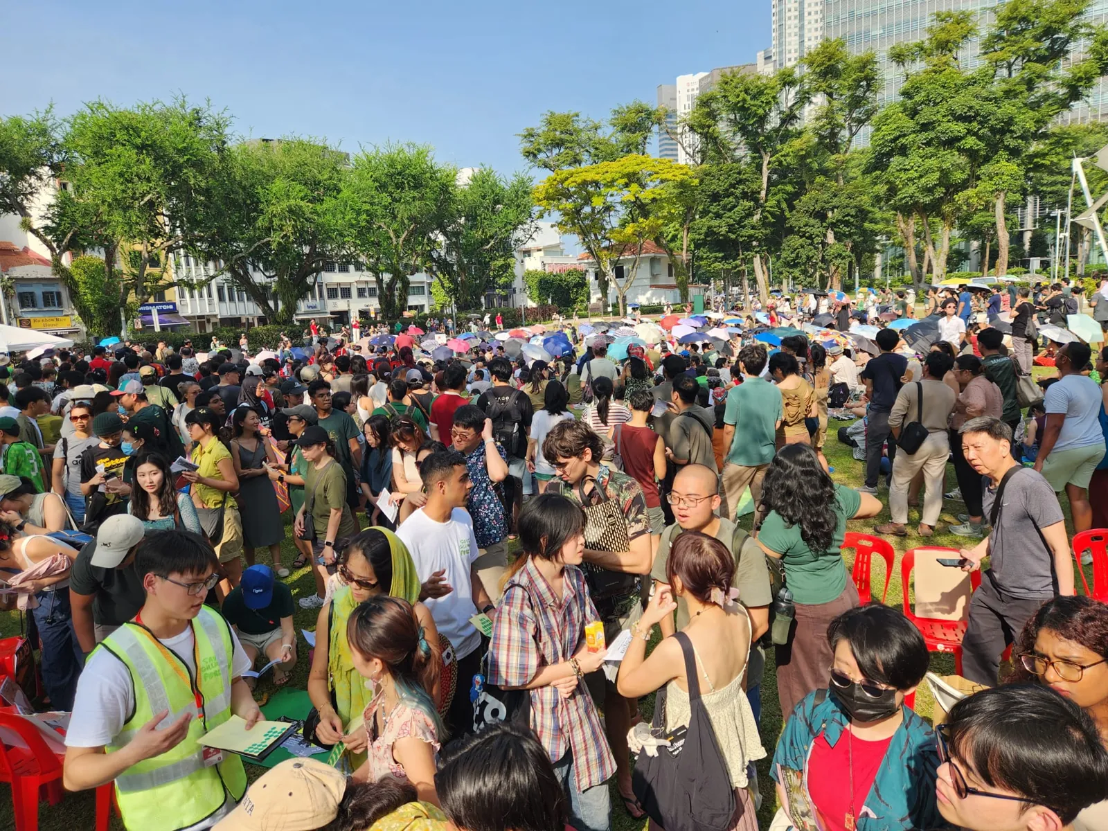 The crowd at Hong Lim Park seen from within, people talking in groups between the booths and the stage