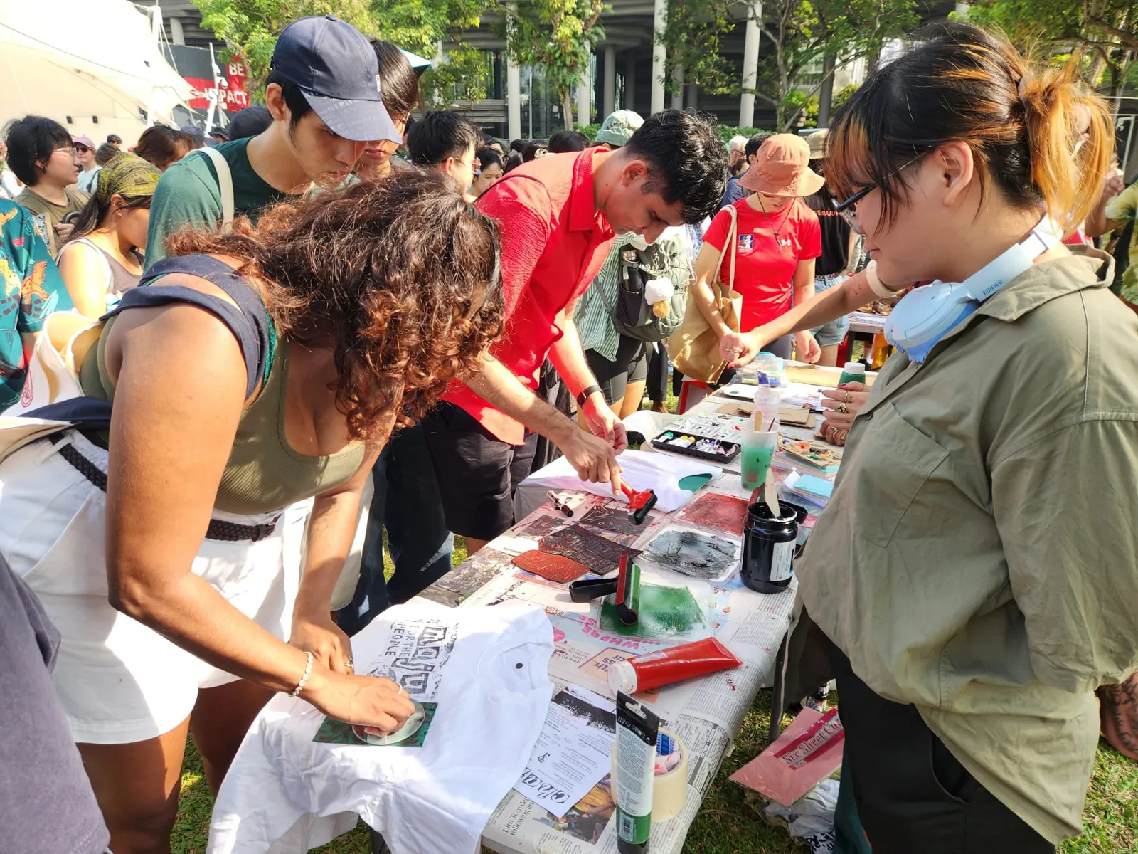 People block-printing t-shirts at a booth table, one shirt reading Maju for the people